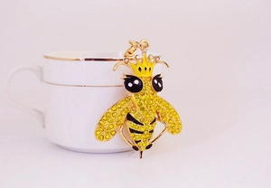 Detalle de un llavero de abeja de cristal dorado con corona colgado en una taza
