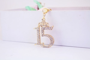 Detail of gold rhinestone number 15 keychain with a small crown on a white gift box