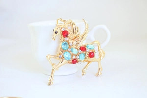 Detaillierte Makroaufnahme von goldenem Pegasus-Anhänger mit blauen und roten Schmucksteinen