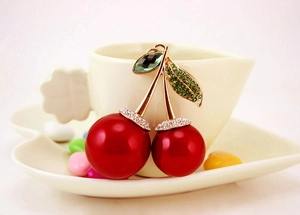 Detail shot of a sparkling cherry pendant with green crystals on a ceramic cup edge