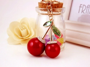 Detailed view of red cherry keychain with gold stem and sparkling green rhinestone leaves