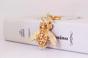 Detalle del llavero de abeja de metal dorado con diseño calado de corazón y corona