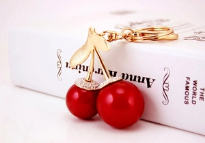 Detail showing red cherry keychain with sparkling rhinestones and golden leaf accent