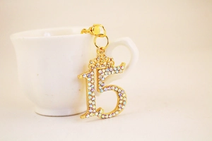Close-up of gold number 15 keychain with small crown and colorful rhinestones on a white cup