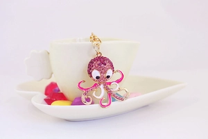 Pink rhinestone octopus keychain with gold-tone alloy frame hanging on a white porcelain cup