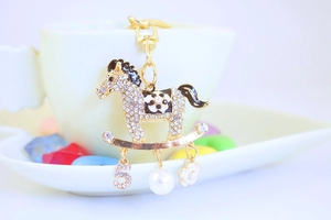 Vue macro porte-clés cheval à bascule doré avec strass et perle sur une tasse blanche