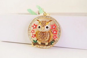 Close-up of owl keychain with brown crystals, pink enamel flowers and gold plating