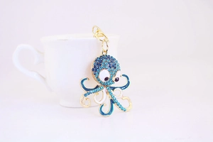Detailed view of golden octopus keychain with light blue rhinestones on a white cup