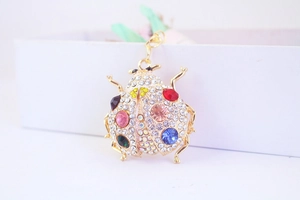 Detail view of colorful rhinestones on a golden ladybug keychain with metal lobster clasp