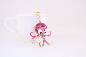 Detail of pink crystal octopus keychain with gold lobster clasp on white coffee cup