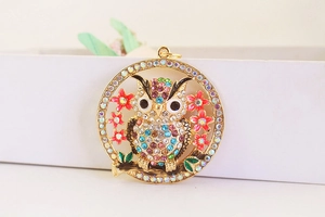 Close-up of golden owl pendant with colorful rhinestones and enamel flower details