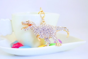 Close-up of a sparkling rhinestone T-Rex dinosaur keychain on a white coffee cup edge