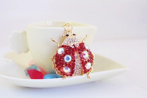 Detail of red rhinestone ladybug keychain hanging on a white coffee cup edge
