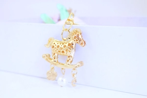 Détail du pendentif cheval à bascule doré avec motifs de cœur et perle blanche
