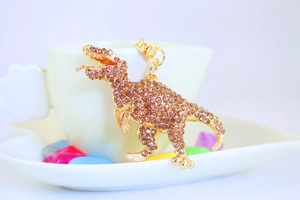 Detailed close-up of a sparkling gold T-Rex dinosaur keychain with amber rhinestones