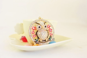 Close-up of crystal owl keychain with pink enamel flowers on a gold-plated base