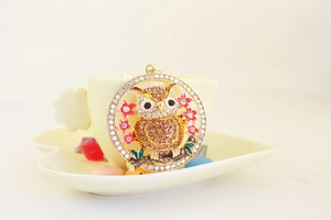 Detailed close-up of a crystal owl keychain with pink enamel flowers on beige background