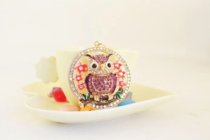 Close-up of owl keychain with purple crystals and pink enamel flowers on a gold base