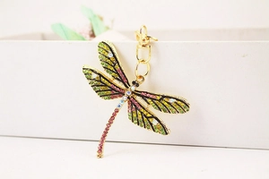 Close-up of golden dragonfly keychain with colorful rhinestones on a white box