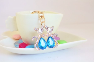 Detail of golden twin cat keychain with blue teardrop crystals and heart-shaped head