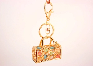 Close-up of golden metal handbag keychain with colorful opal stones and floral cutout detail