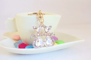 Detail of golden twin cat keychain with sparkling crystals on a white ceramic cup