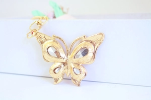 Detail of a golden butterfly keychain with crystal wings and a metal lobster clasp