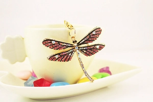 Detailed view of a gold dragonfly keychain with red and AB crystals on a white cup