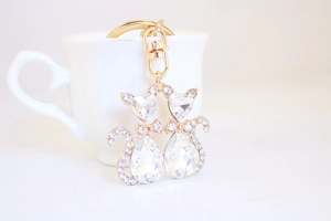 Close-up of golden twin cat keychain with crystals hanging on a white coffee cup
