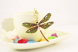 Detailed close-up of a golden dragonfly keychain with colorful rhinestones on a white cup