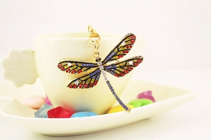 Macro detail of colorful dragonfly keychain with crystals hanging on a white ceramic cup