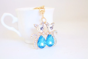 Detail of cute cat keychain with blue heart crystals leaning on a white ceramic cup