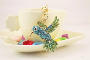 Détail d'un porte-clés colibri avec cristaux bleus et verts sur une base dorée