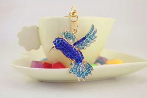 Détail d'un porte-clés colibri doré avec cristaux bleus sur le bord d'une tasse