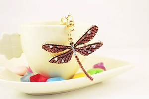 Detailed close-up of a dragonfly keychain with red and white rhinestones on golden alloy
