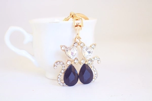 Detail of elegant dual cat keychain with white crystal heads and black gemstone bodies