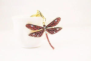 Detailed view of colorful rhinestone dragonfly keychain hanging on a white porcelain cup