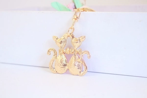 Detail of two golden cat-shaped metal keychains with bow tie and lobster clasp