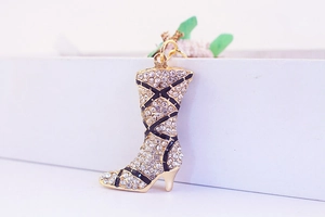 Close-up of golden boot keychain with crystal rhinestones and black striped enamel details