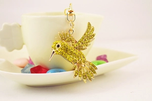 Détail d'un porte-clés colibri aux cristaux jaunes et verts sur une tasse blanche
