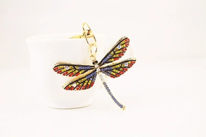 Close-up of a golden dragonfly keychain with colorful rhinestones on a white cup