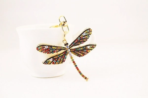 Close-up of colorful rhinestone dragonfly keychain hanging on a white ceramic cup edge