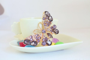 Dettaglio di un portachiavi a farfalla dorato con cristalli viola su una tazza di ceramica