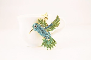 Détail du porte-clés colibri avec strass bleus et verts sur une monture dorée élégante