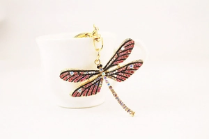 Macro shot of colorful rhinestone dragonfly keychain hanging on a white ceramic cup