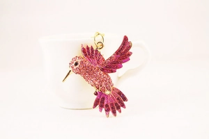 Détail d'un pendentif colibri en strass rose scintillant sur une tasse en céramique