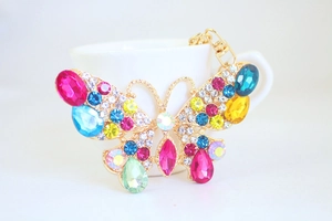 Dettaglio portachiavi a farfalla con strass colorati appoggiato sul bordo di una tazza