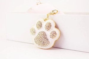 Detail view of a gold-trimmed white enamel paw print keychain with sparkling rhinestones