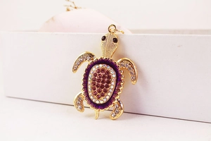 Détail macro d'un pendentif tortue en cristal avec des strass violets et blancs