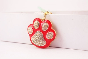 Macro detail of red enamel cat paw keychain with sparkling white rhinestones and gold plating